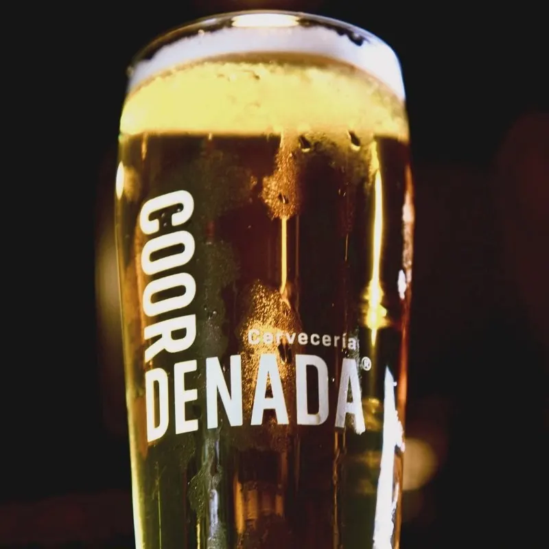 Vaso de cerveza dorada con el logo de Coordenada